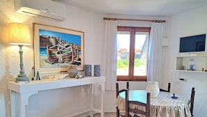 Uma sala de jantar com mesa, cadeiras, um quadro, luminária e janela com cortinas.