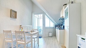 Eine Küche mit weißen Schränken, einem Esstisch mit Stühlen und einem Fenster mit Blick auf einen Balkon.