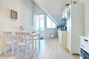 Una cocina con armarios blancos, una mesa de comedor con sillas y una ventana con vista a un balcón.