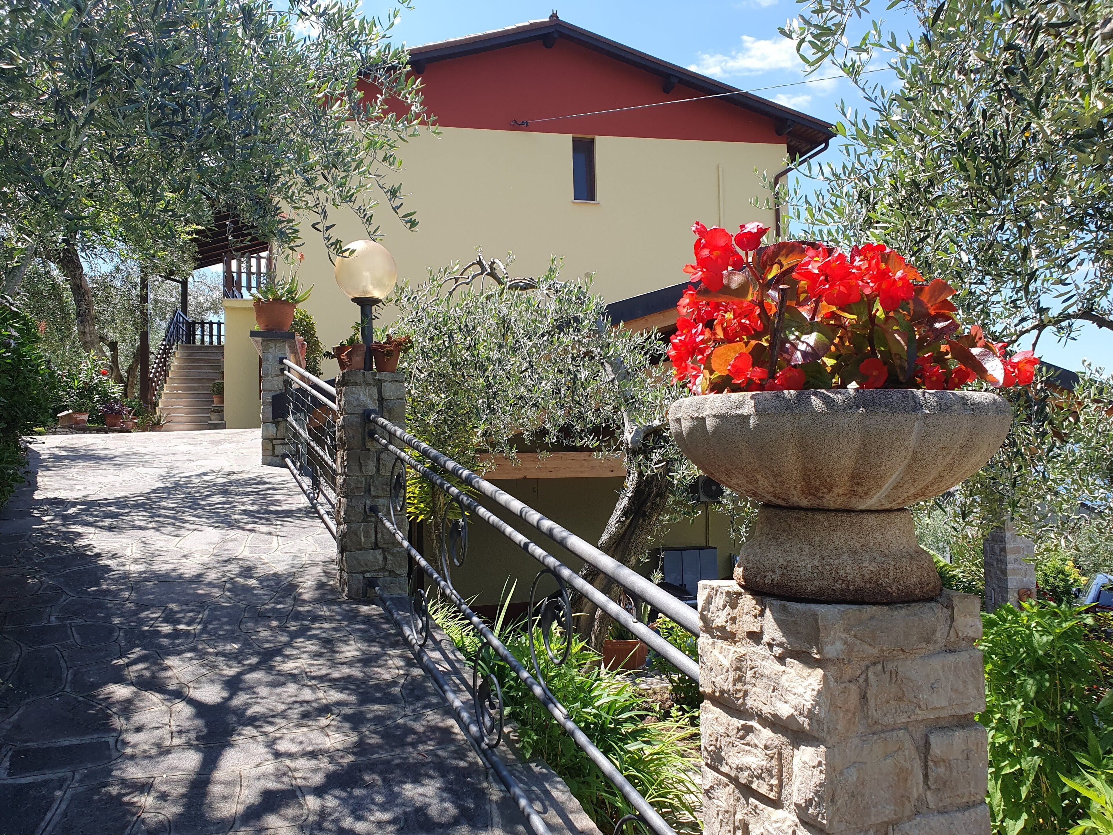 A stone pathway leading to a building with a red roof, surrounded by greenery and potted plants.