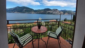 En balkon med et bord og stole, med udsigt over en sø og bjerge.