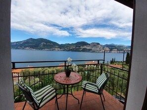 Un balcón con una mesa y sillas, con vista a un lago y montañas.