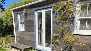 Uma casa de madeira com um alpendre, incluindo uma mesa e cadeiras de metal, cercada por cascalho e plantas em vasos.