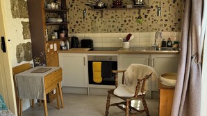 Uma cozinha acolhedora com parede de pedra, prateleiras de madeira e um espaço de refeições com mesa listrada e uma cadeira.