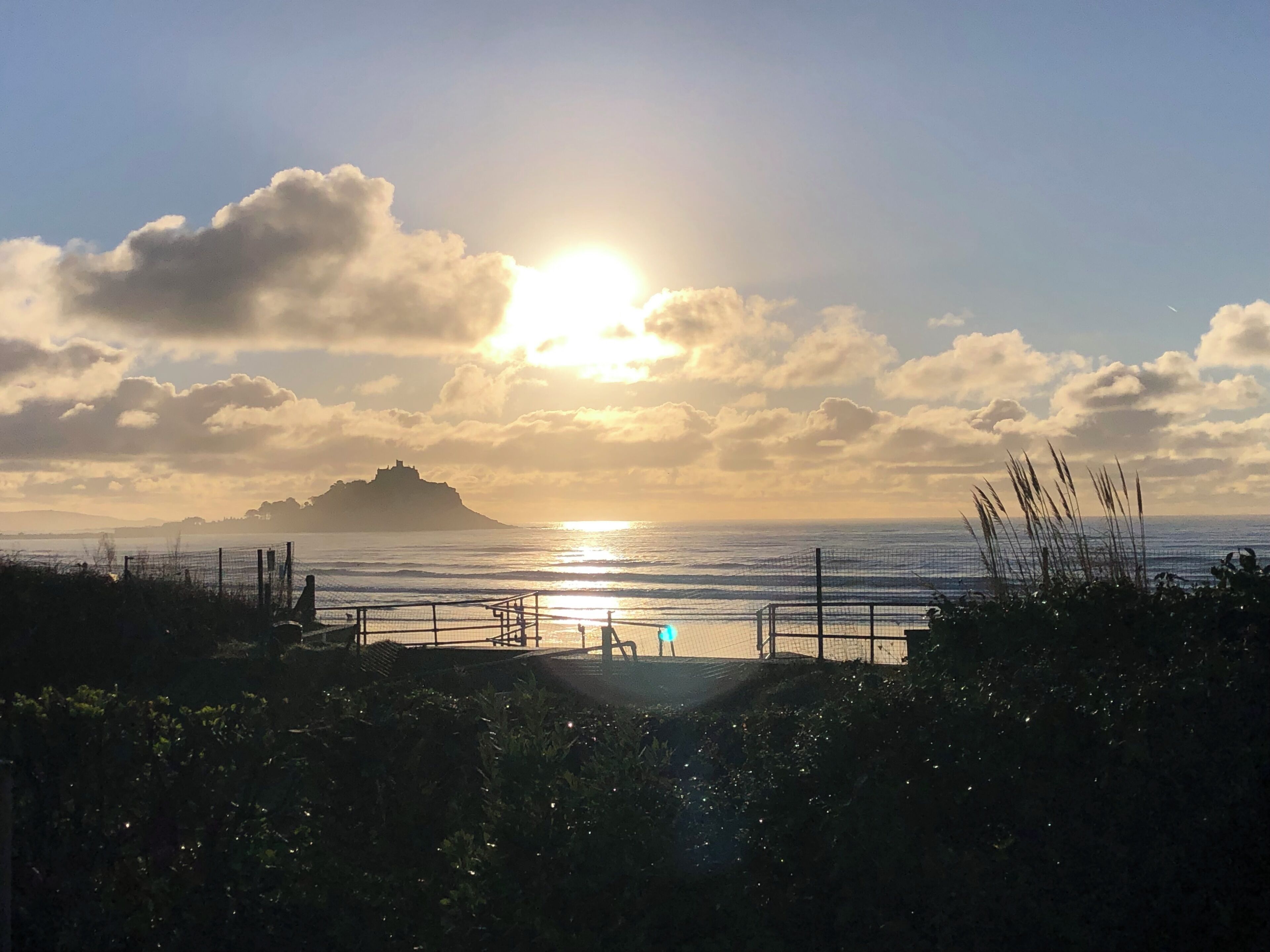 Vista costeira com uma ilha distante, uma vedação e uma pessoa de pé junto ao corrimão.