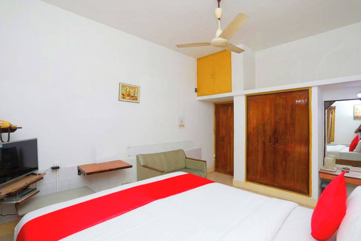 Habitación de hotel con cama, televisión, escritorio, silla, ventilador de techo y armario.