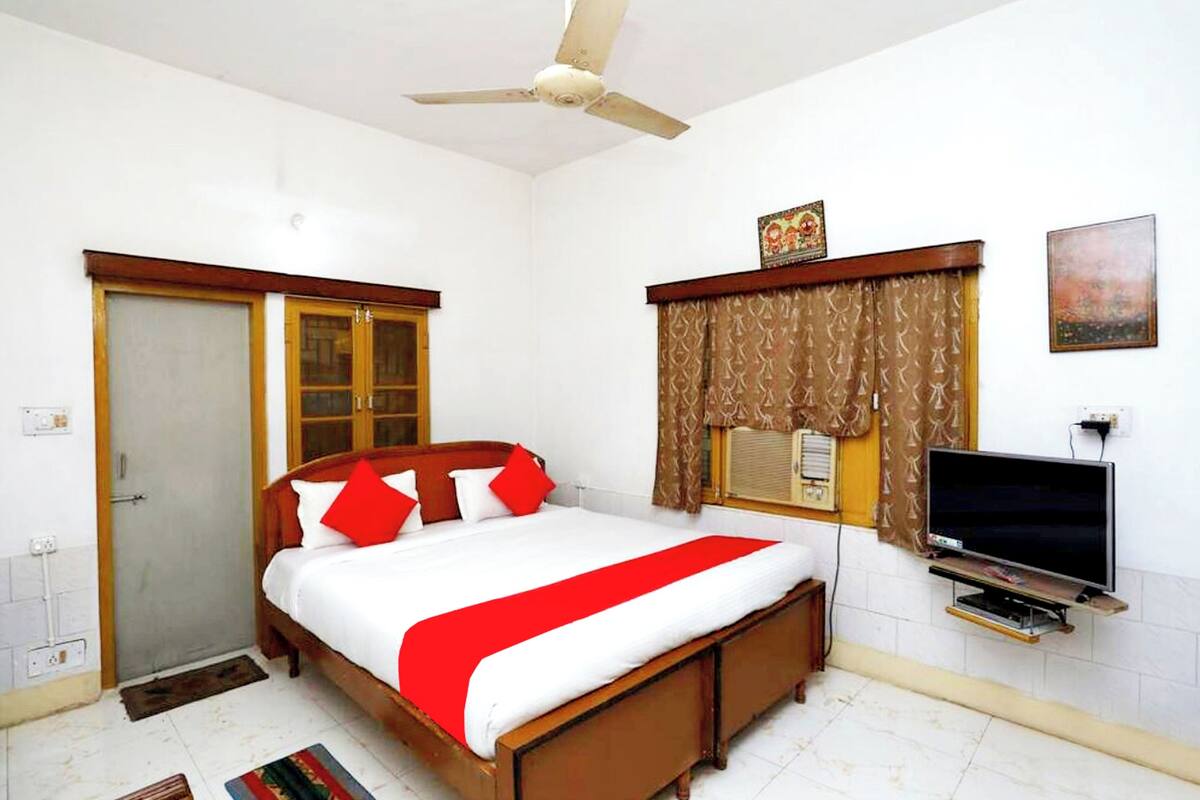Un dormitorio con cama, ventilador de techo, televisor y ventana con cortinas.