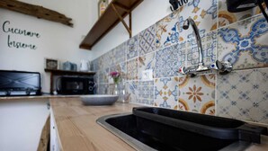 Eine Küche mit Holzarbeitsplatte, einem schwarzen Spülbecken, einer Mikrowelle und einer gefliesten Rückwand mit Blumenmuster.