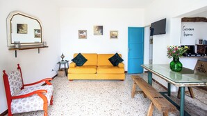 Ein Wohnzimmer mit einer Couch, einem Sessel, einem Tisch, einem Deckenventilator, einem Fernseher und einer blauen Tür.