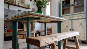 Un banco de madera rústico con estructura de metal verde, suelo de baldosas y un aparador antiguo al fondo.