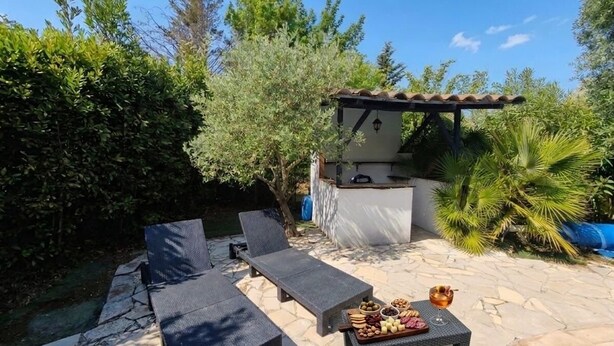 Een terras met lounge fauteuils, een tafel met lekkernijen, een barbecue en een zwembad.