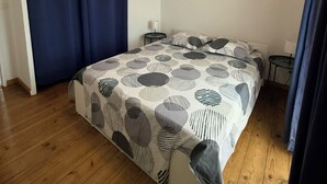 Een slaapkamer met een bed, gordijnen, een nachtkastje en een lamp.