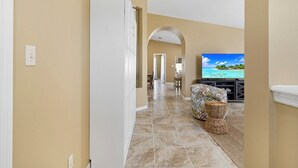 A hallway leading to a living area with a television displaying a tropical beach scene. - Seabreeze- Private Pool and just steps to Beach (St. Augustine Beach)