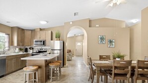 A modern kitchen with a central island, stainless steel appliances, and a dining area with wooden chairs and a table. - Seabreeze- Private Pool and just steps to Beach (St. Augustine Beach)