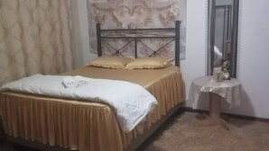 A bedroom with a bed, a bedside table with a clock, and a wall with floral patterns.