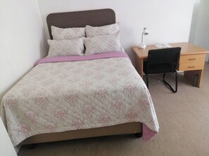 A bed with a floral quilt, a bedside table with a lamp, and a chair. - Room-charming B&B Retreat in Viljoenskro (Moqhaka)
