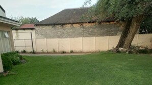 A well-maintained grassy backyard with a brick wall, a tree, and a building with a red roof.