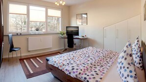 Ein Schlafzimmer mit Bett, Schreibtisch, Stuhl, Heizkörper und einem Fenster mit Jalousien.