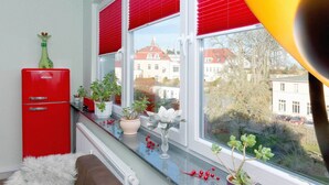 Eine Küche mit einem roten Kühlschrank, Blumentöpfen auf der Fensterbank und Blick auf Gebäude im Freien.