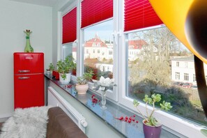 A kitchen with a red refrigerator, potted plants on the windowsill, and a view of buildings outside. - Vacation apartment near the beach in Zinnowitz with roof terrace (Zinnowitz)