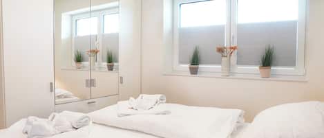 A hotel room with a large mirror, two beds, a window with blinds, and potted plants.