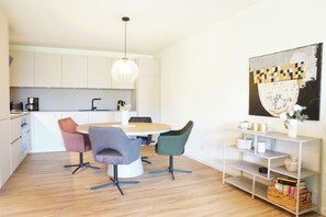 Une cuisine moderne avec une table de salle à manger ronde, quatre chaises, un luminaire suspendu et une bibliothèque agrémentée d’objets décoratifs.