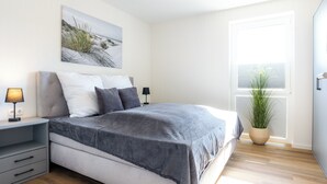 Ein modernes Schlafzimmer mit Bett, Nachttischen, einem Tisch für Kleinigkeiten, einer Zimmerpflanze und einem Fenster mit Jalousien.