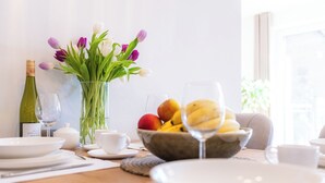 Ein Esstisch ist gedeckt mit Tellern, einer Obstschale, einer Weinflasche und einem Blumenstrauß.