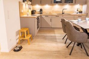 Une cuisine moderne avec des meubles en bois, un tabouret en bois, une table à manger avec des chaises et un coin repas pour animaux de compagnie.