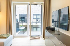 A modern hotel room with a large TV, a sofa, a balcony with a table and chairs, and a sliding glass door. - Vacation apartment Hyggehuus Tossens - Balcony. Sauna. Close to the beach. (Tossens)