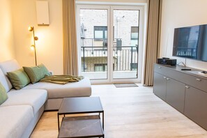 Un salon moderne comprenant un canapé, une table basse, un téléviseur et un balcon offrant une vue sur les immeubles.