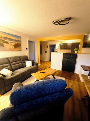 A living room with a sofa, a blue chair, a wooden coffee table, and a chalkboard with a welcome message. - North Sea dreams Scheper - Anchorage (Jever)