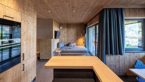 A compact room with a wooden ceiling, a bed, a small table, and a built-in oven. - MOAHOF Chalets & Appartements (Wagrain)