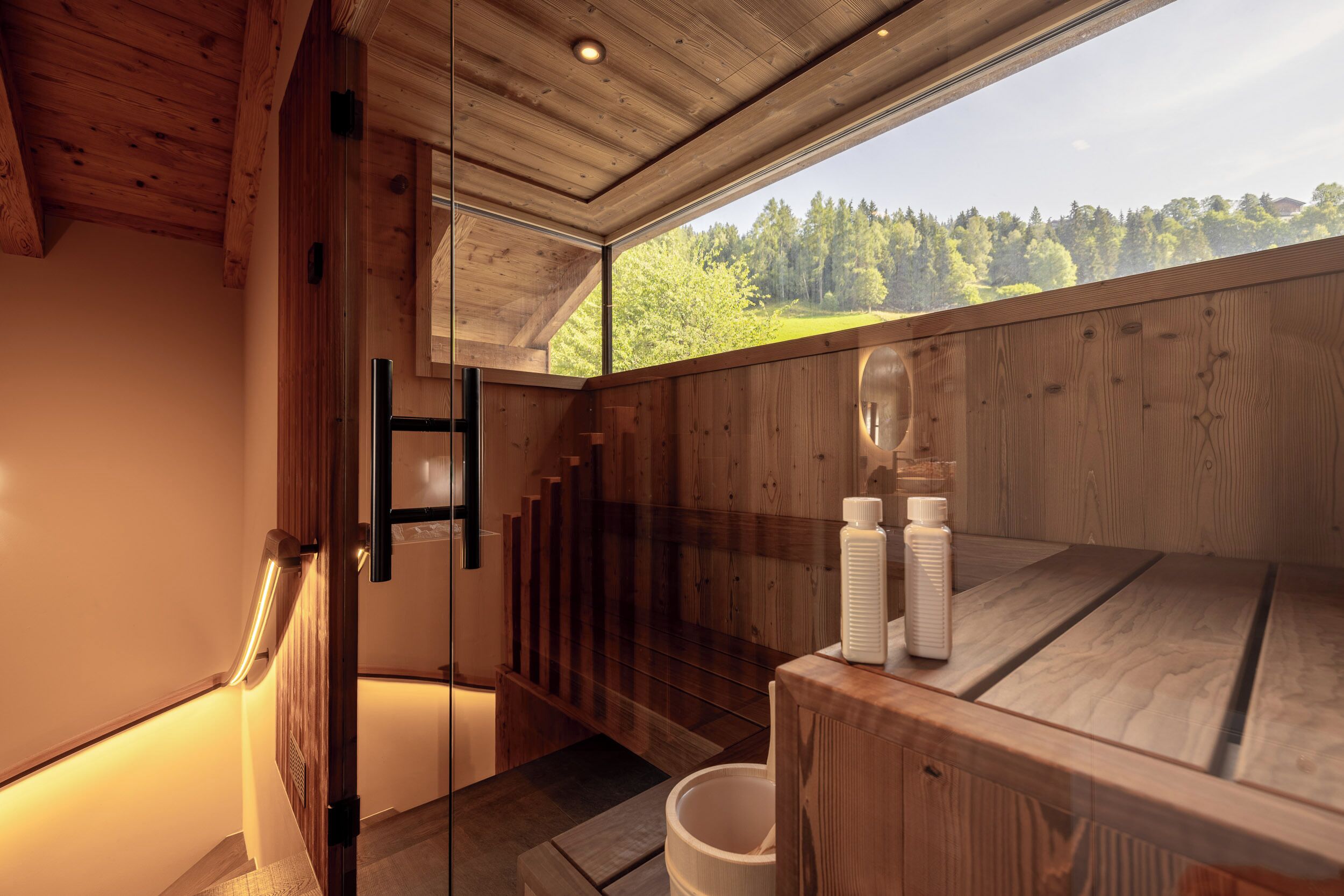 A wooden interior with a glass door leading to a balcony, a wooden bench, and two bottles on a table.