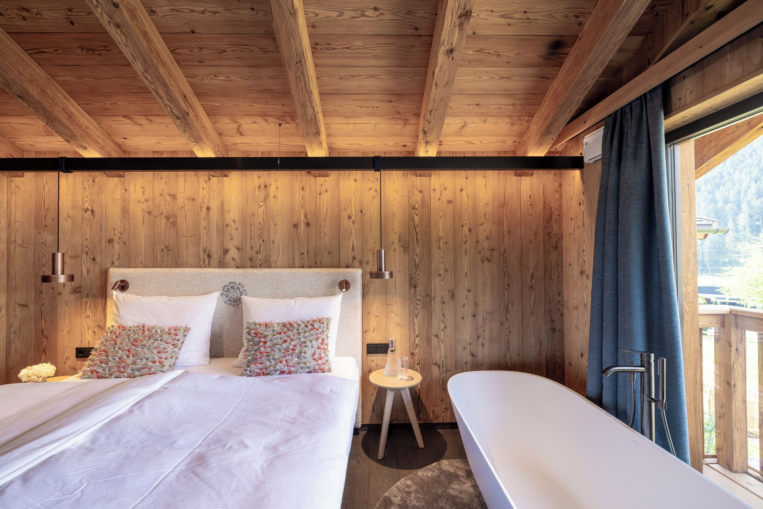A wooden cabin bedroom with a bed, bedside tables, and a view of the outdoors.