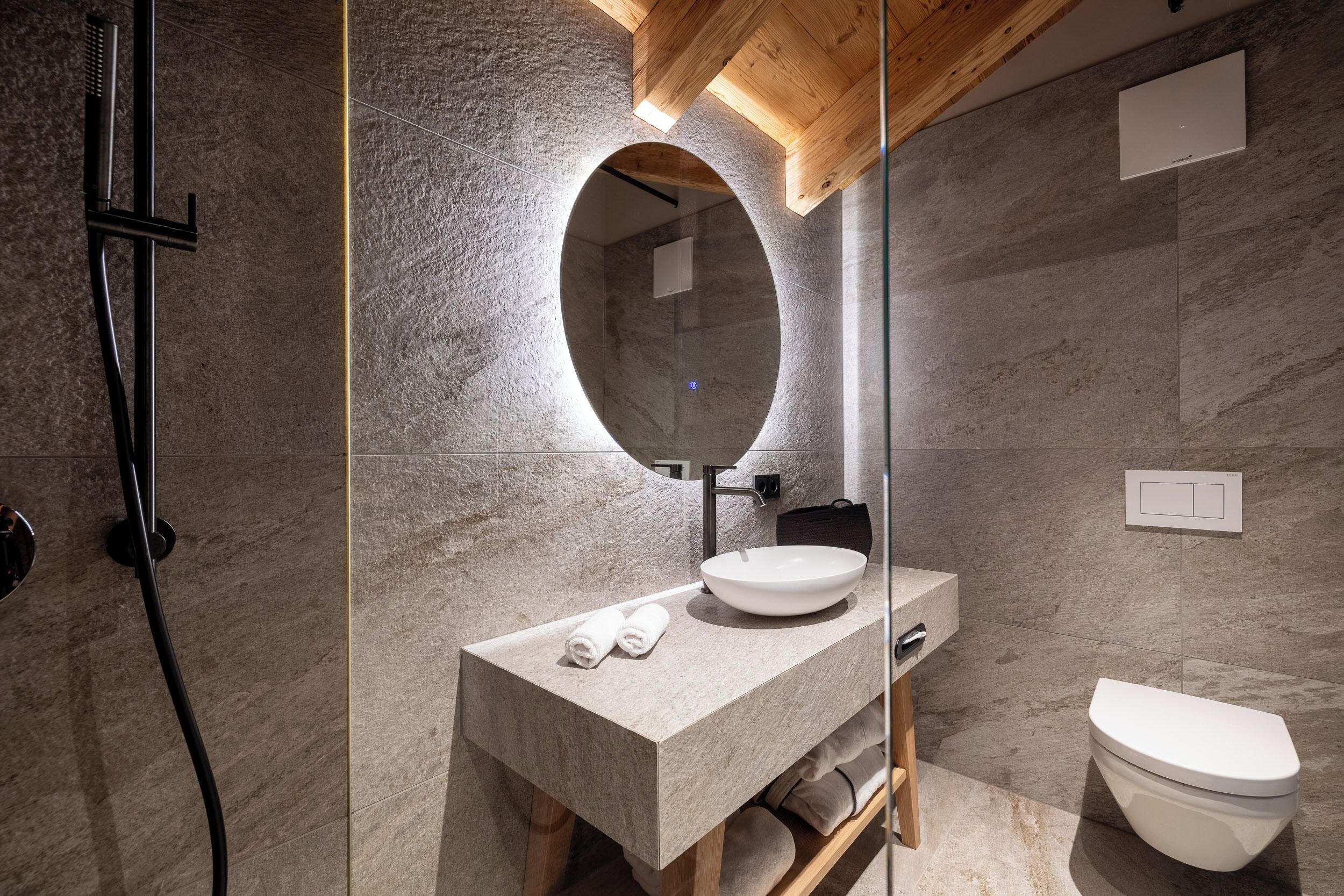 Ein modernes Badezimmer mit einer Naturstein-Arbeitsplatte, einem runden Spiegel, einem weißen Waschbecken und einer Toilette.