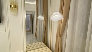 A room with a tufted bench, a mirror, a wall-mounted lamp, and a large mirror reflecting a hallway. - Suites within walking distance of Lake Como (Como)