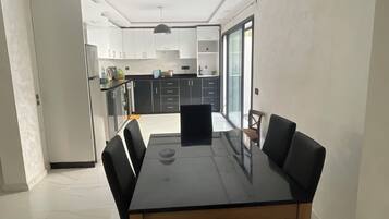 Una cocina moderna con armarios blancos, encimera negra y un comedor con mesa de vidrio y sillas negras.