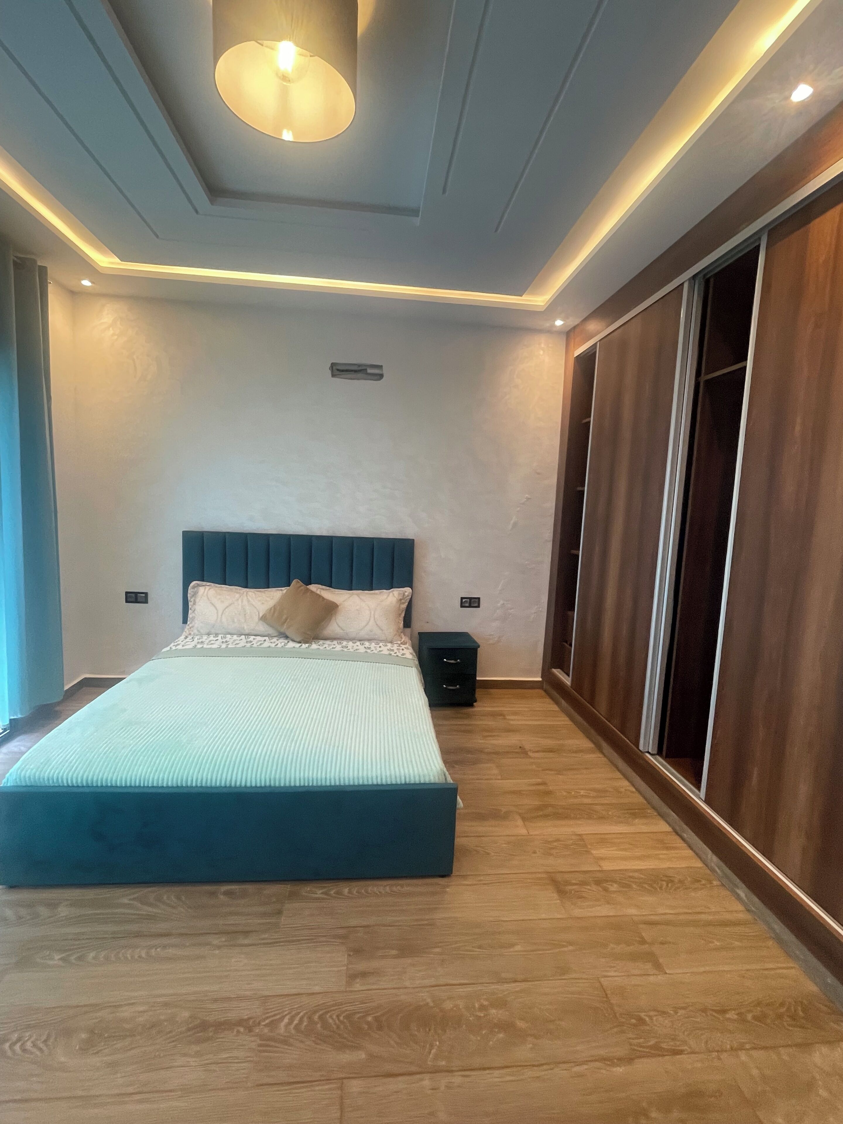 A bedroom with a bed, bedside tables, a wardrobe, and a ceiling light fixture.