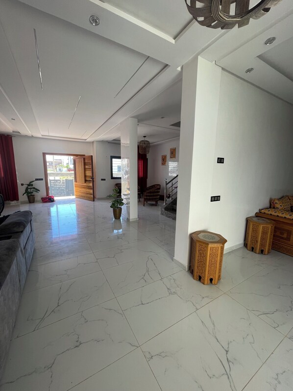 A spacious living area with a high ceiling, a sofa, a coffee table, a potted plant, and a staircase leading to another level.