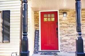 A red door with a 'WELCOME' sign, a stone wall, and black columns. - KC World Cup-Game Day Stay-1 min to Arrowhead (Kansas City)