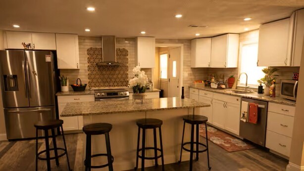 Una cocina moderna con una isla central, taburetes de bar, electrodomésticos de acero inoxidable y un salpicadero decorativo.
