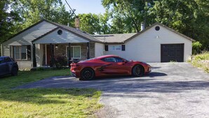 Un coche deportivo rojo estacionado frente a una casa de dos pisos con garaje.