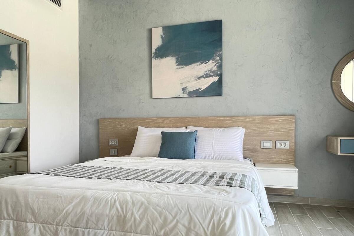 Ein modernes Schlafzimmer mit einem großen Bett, einem Holz-Kopfteil, einem Wandbild, einem Nachttisch und einem runden Spiegel.