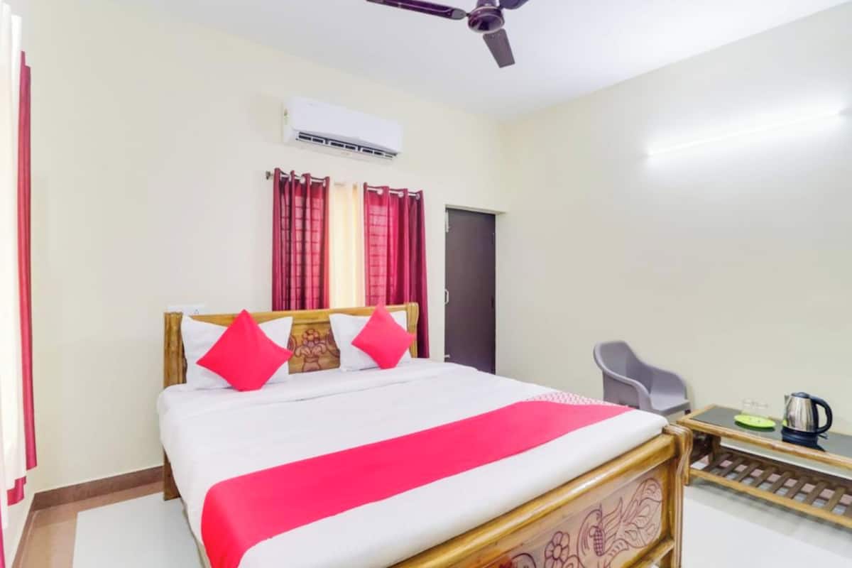 Une chambre d’hôtel équipée d’un lit, d’un ventilateur de plafond, d’un climatiseur, d’un bureau avec une bouilloire et d’une chaise.