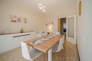 A dining area with a long wooden table, white chairs, a wall-mounted lamp, and artwork. - Casa Lella - Apartment for up to 6 people for families and group of friends (Novara)