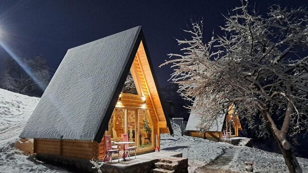 A wooden cabin with a sloped roof, a small porch, and a lit interior.