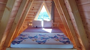 A wooden attic bedroom with a bed, pillows, and a window.