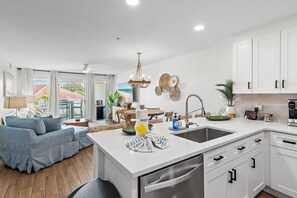 A modern kitchen with white cabinets, a central island, stainless steel appliances, and a dining area with a blue sofa. - New at Maravilla • Gulf View Balcony • Free Beach Service • Sleeps 8 (Miramar Beach)