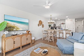 A living room with a large TV, wooden cabinet, dining area, and a kitchenette. - New at Maravilla • Gulf View Balcony • Free Beach Service • Sleeps 8 (Miramar Beach)